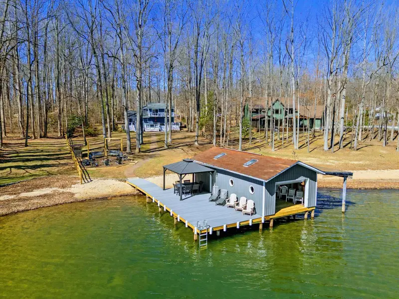 From Above - An aerial view shows the full dock and boathouse structure, sandy beach, and the spacious flat yard leading up to the house.