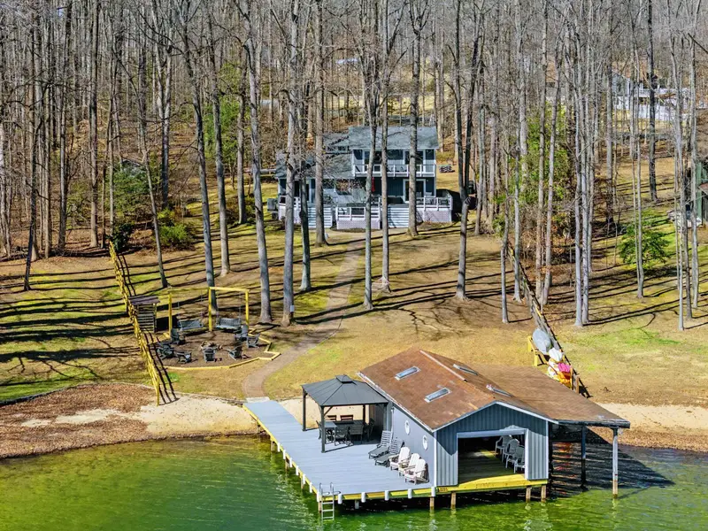 Full Property Aerial - The house sits among tall trees above the boathouse and dock, with the fire pit, flat yard, and lake all in view.