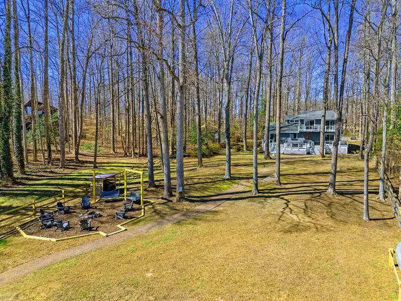 Full Yard - A bird's-eye view captures the flat, open yard with the ninja course, fire pit circle, bench swings, and lake beyond.