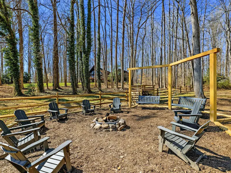 Fire Pit and Swings - Bench swings and Adirondack chairs ring the fire pit, with the house visible through the tall trees.