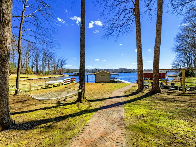 Hammock and Path - A hammock strung between tall trees sits along the brick path to the lake, with the boathouse visible ahead.
