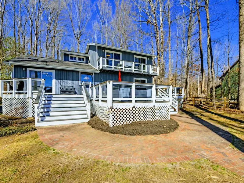 Lake-Side Exterior - The blue-gray home features multiple levels of decking, white railings, and a basketball hoop, with the lake just down the hill.