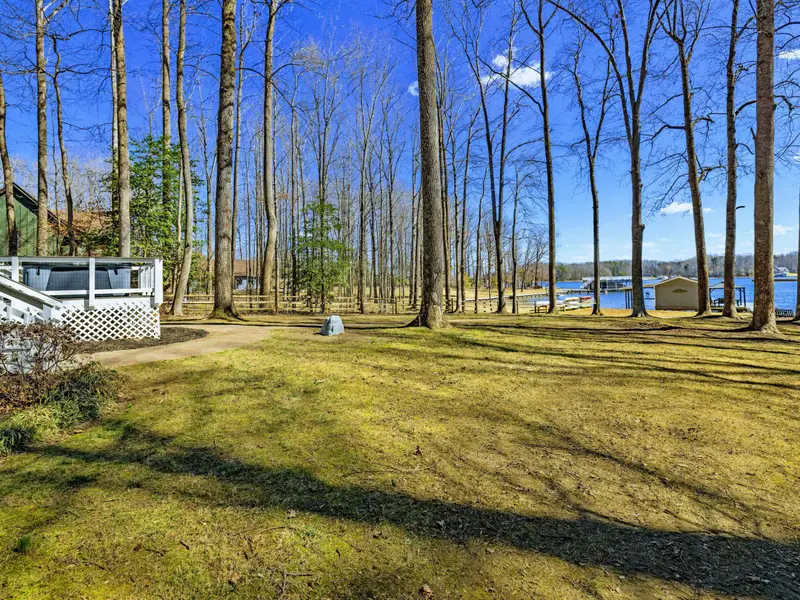 Flat Yard - The open, level yard is ideal for cornhole, frisbee, or any lawn game, with the lake and boathouse visible through the trees.