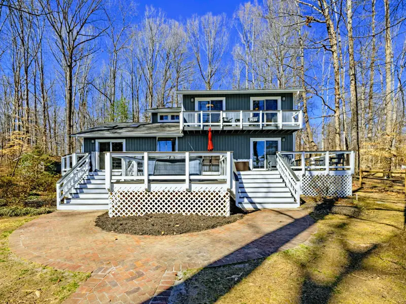 Welcome Home - The two-story exterior with white wraparound decks, a red front door, and tall surrounding trees greets guests on arrival.