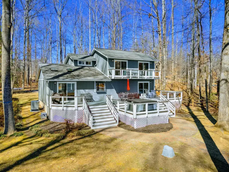 Rear Exterior - Multiple levels of decking wrap around the back of the house, connecting the hot tub, outdoor dining, and lake views into one seamless outdoor space.