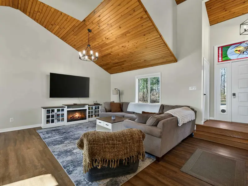 Living Room - The vaulted ceiling with warm wood planks opens up the space, with a stained glass front door and staircase to the upper level adding character.