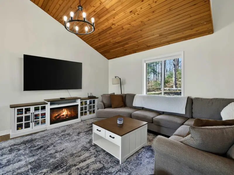 Living Room - A large sectional, 75-inch Roku TV, electric fireplace, and vaulted wood-plank ceiling set the scene for cozy movie nights after a day on the lake.