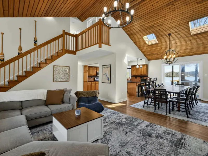 Open Floor Plan - The living room, dining area, and kitchen flow together under a vaulted wood-plank ceiling with skylights, oar decor, and a Lake Anna map on the wall.