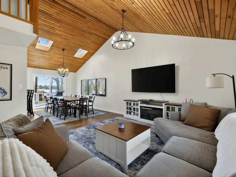 Great Room - Skylights flood the vaulted ceiling with natural light, connecting the sectional lounge, dining table, and sliding doors to the lake-facing deck.