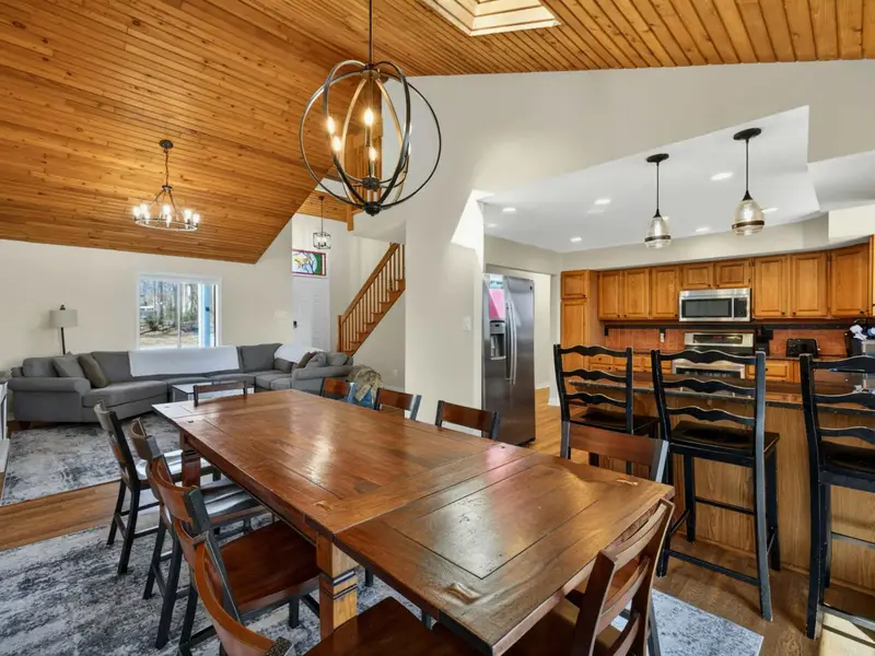Dining Area - A large wood farm table seats 10 under an orb chandelier, with bar seating for 3 more at the kitchen island and the vaulted ceiling soaring overhead.