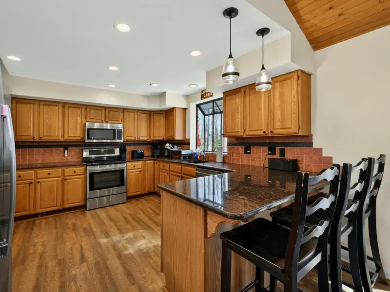 Kitchen - Oak cabinets, granite countertops, stainless steel appliances, and pendant-lit bar seating for 3 make cooking for the group easy and social.