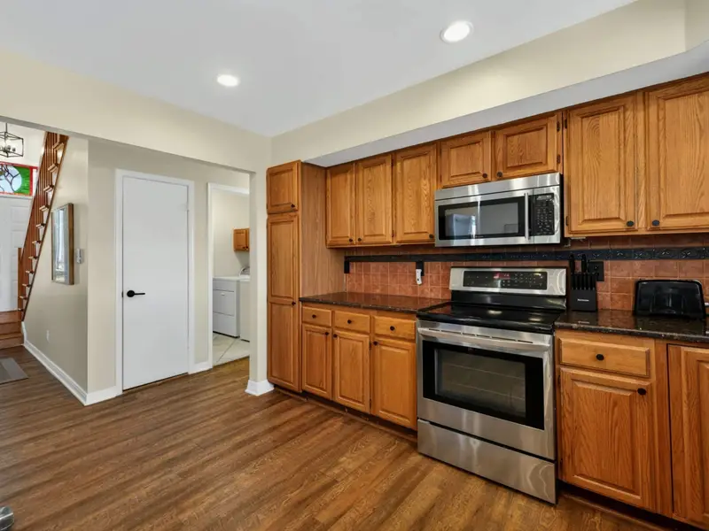 Kitchen and Entry - Stainless appliances and warm oak cabinets fill the kitchen, with the stained glass front door and staircase visible from the cooking area.