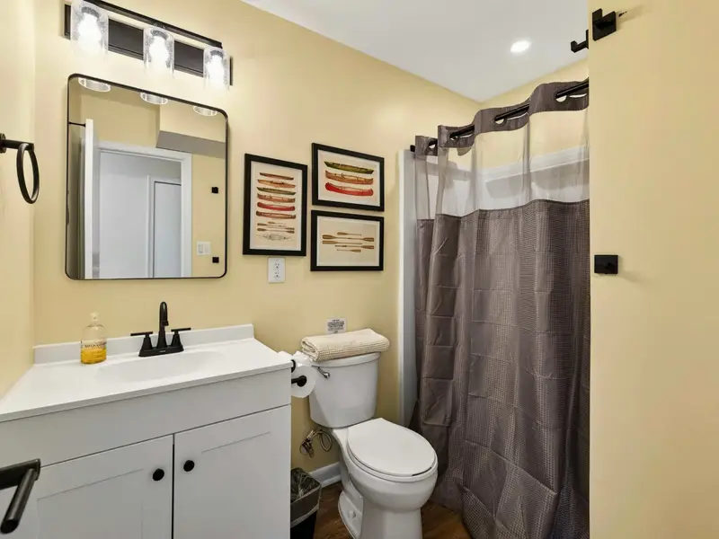 Main-Level Bath - A full bathroom with white vanity, black fixtures, and canoe artwork sits conveniently on the main floor near the kitchen and bedroom.