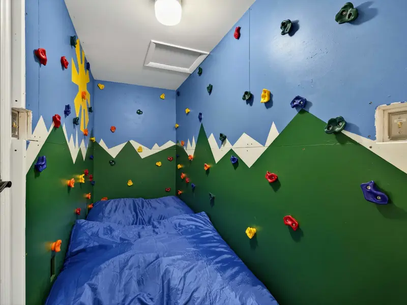 Rock Climbing Room - A mountain mural with colorful climbing holds covers the walls, with a blue crash pad below for safe landings.