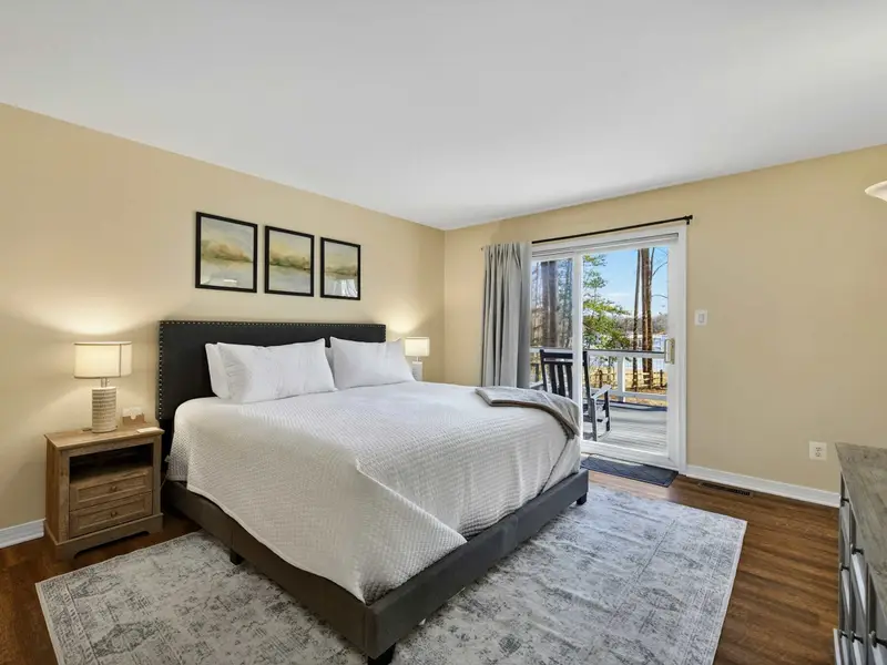 Primary Suite - A king bed with crisp white linens and watercolor art sits beside a sliding door that opens directly onto the deck with lake views.