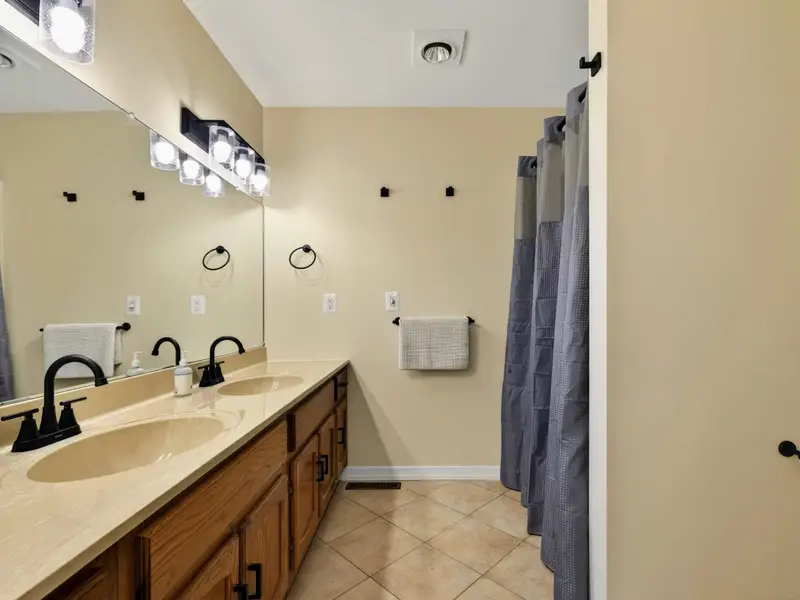 Ensuite Bath - A double oak vanity with black fixtures and a wide mirror serves the primary bedroom, with a shower just steps away.