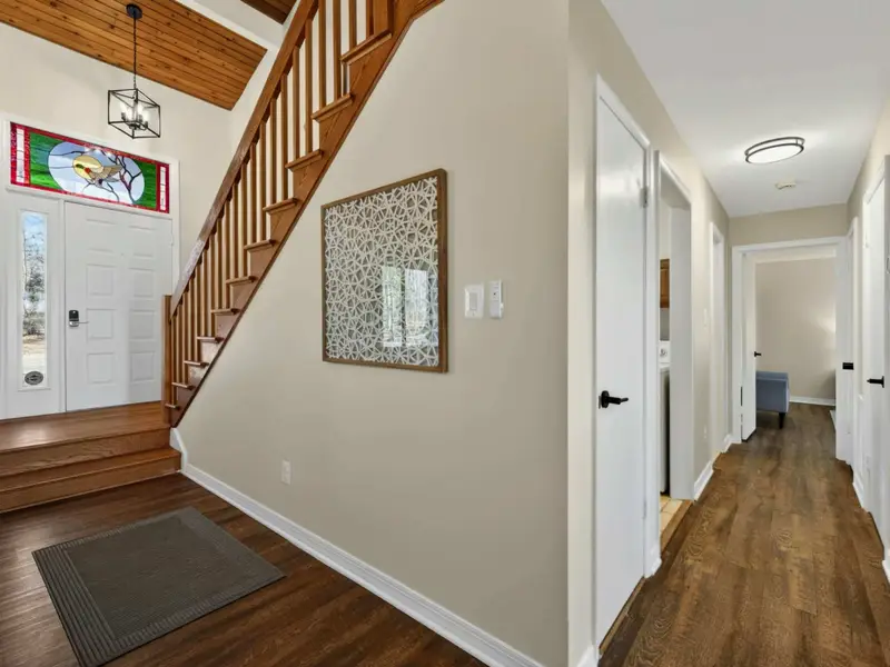 Entry and Hallway - A stained glass front door with a bird design and a warm wood staircase welcome guests, with the hallway leading to bedrooms and bathrooms.