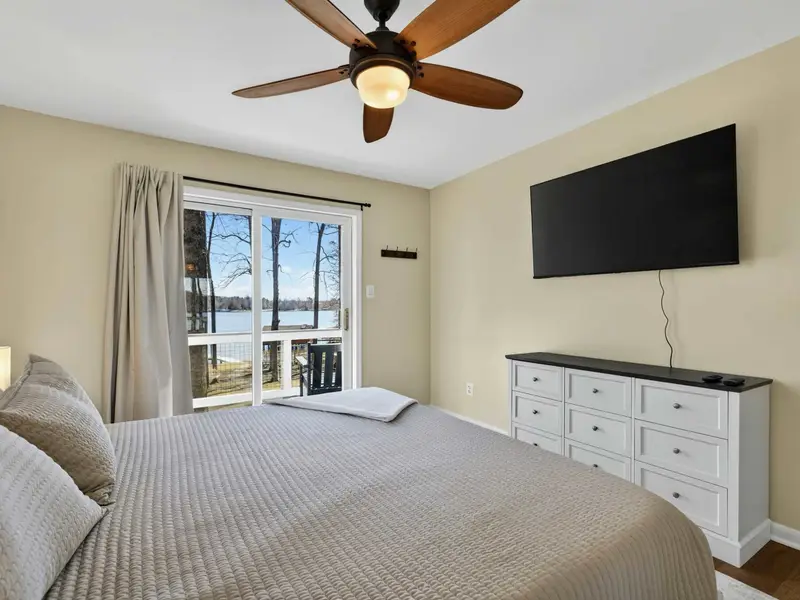 Upper Bedroom - A wall-mounted TV and dresser round out the room, with lake and deck views through the sliding door.