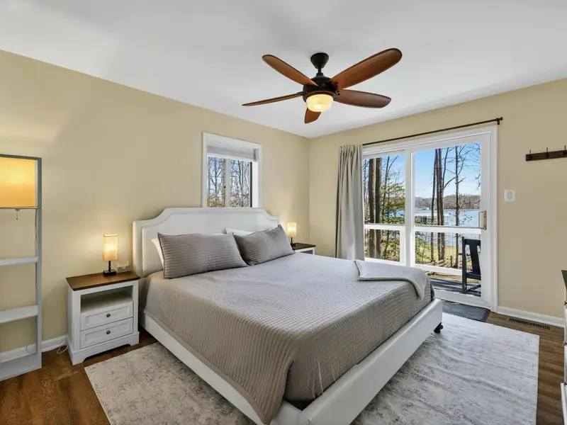 Upper Bedroom - A king bed, ceiling fan, and sliding door to a private balcony with bistro seating and lake views through the trees.