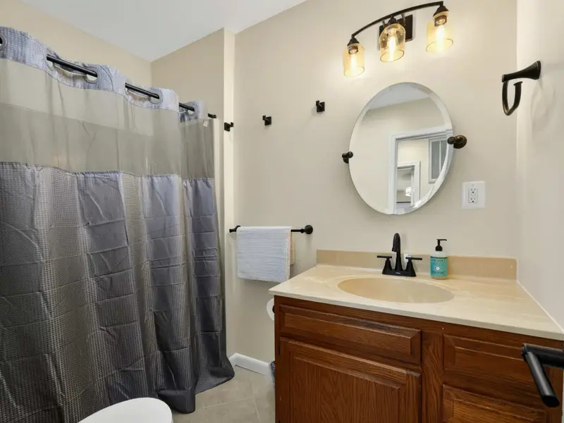 Upper Hall Bath - Oak vanity, round mirror, and black fixtures give this full bath a clean, modern feel.