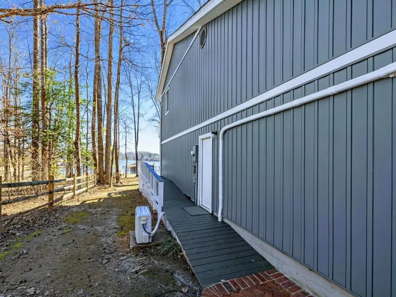 Side Exterior - A walkway along the house leads toward the lake, visible through the trees.