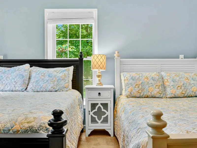 Queen bed with botanical bedding and a garden view. The lower level bedrooms stay cool and quiet.