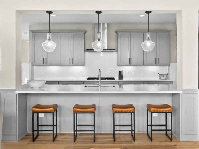 Kitchen - Four leather bar stools line the island beneath pendant lights, a casual spot for coffee or evening drinks.