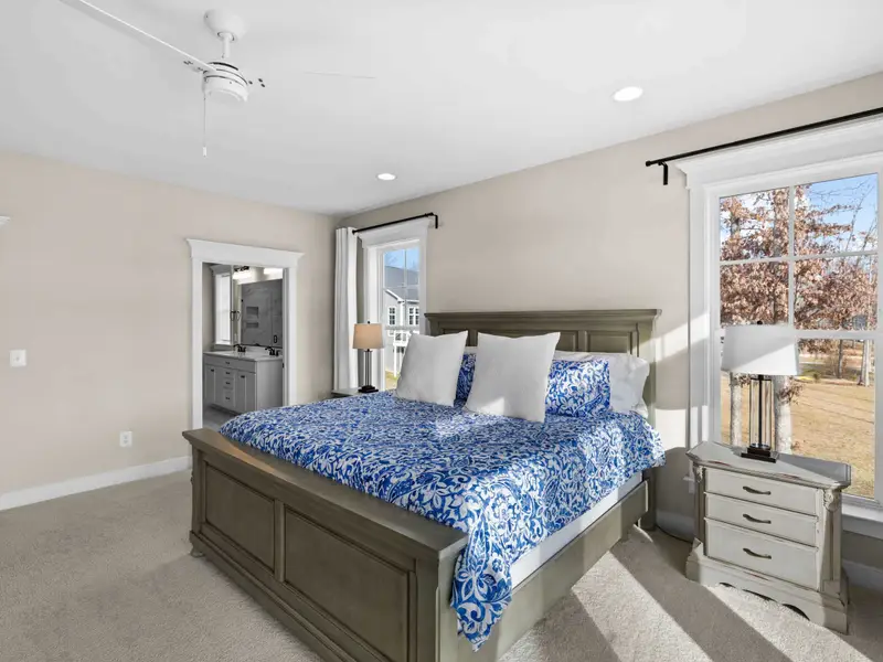 Primary Suite - The primary bedroom from the corner, showing the king bed, TV, ceiling fan, and ensuite doorway.