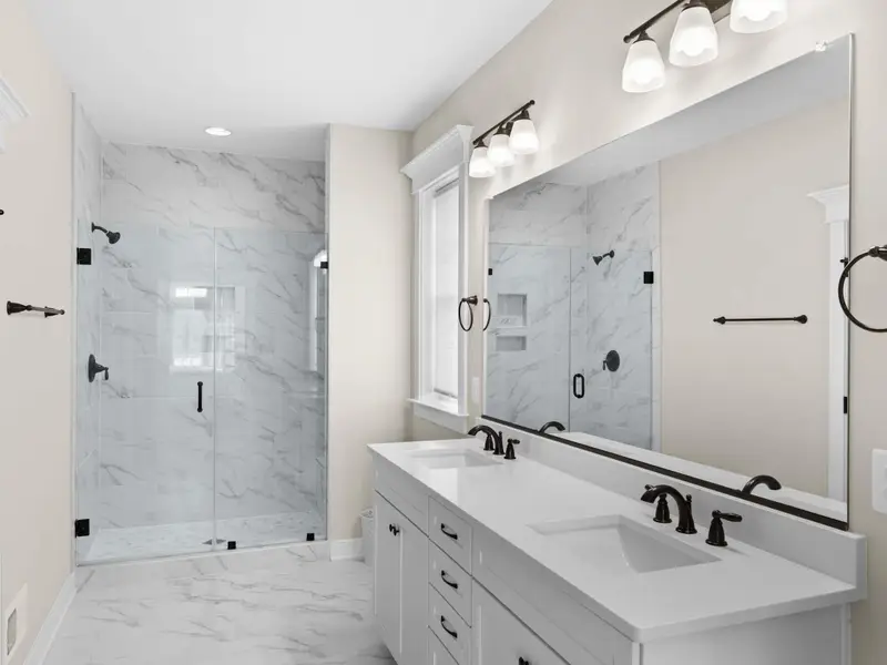 Primary Bathroom - A marble-tiled walk-in shower with glass door, matte black fixtures, and a built-in niche.