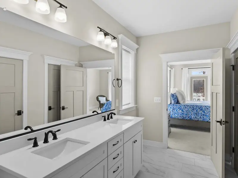 Primary Bathroom - The double vanity with white cabinetry and quartz countertop, with the king bed visible through the doorway.