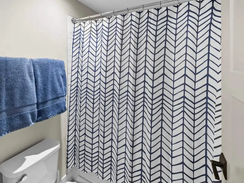 Bathroom - The en-suite bath serving the upper bedrooms, with a tub-shower combo and striped curtain.