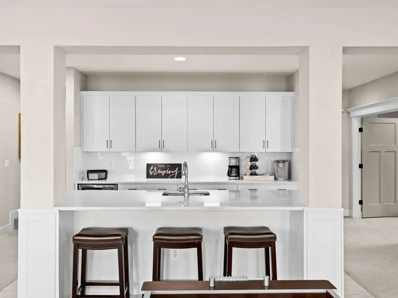 Lower Level Bar - Bar island with three stools, quartz countertop, and a 'Love is Brewing' sign over the coffee maker.