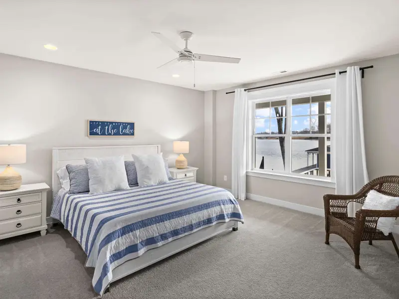 King Suite - A lower-level king bedroom with ceiling fan, wicker chair, and an 'at the lake' sign above the headboard.