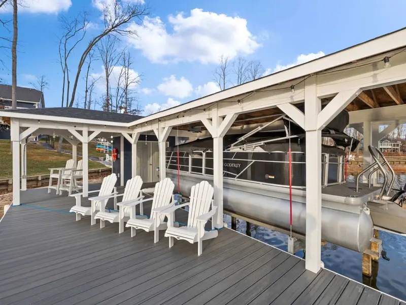 Boathouse - A pontoon boat on the lift under the covered slip, with Adirondack chairs on the deck beside it.