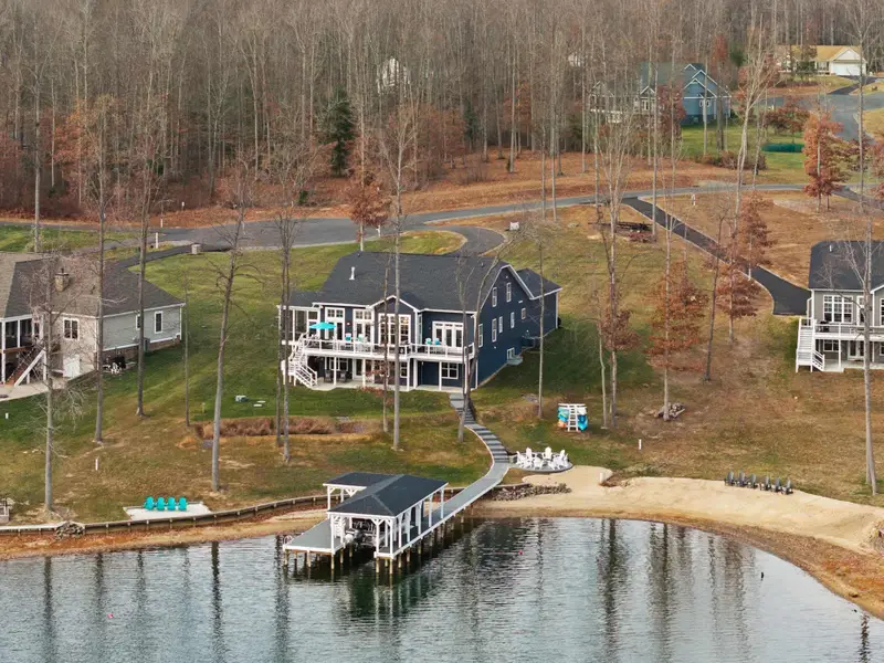 Exterior - Aerial from the lake side shows the blue house, fire pit area, dock, and boathouse together.
