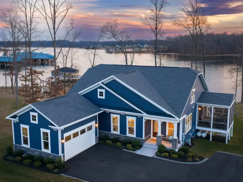 Exterior - A sweeping twilight aerial shows the full front elevation, garage, screened porch, and lit boathouse behind.