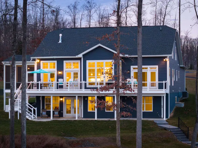 Exterior - The full rear elevation at dusk, upper deck and lower patio both lit, the lake going dark below.