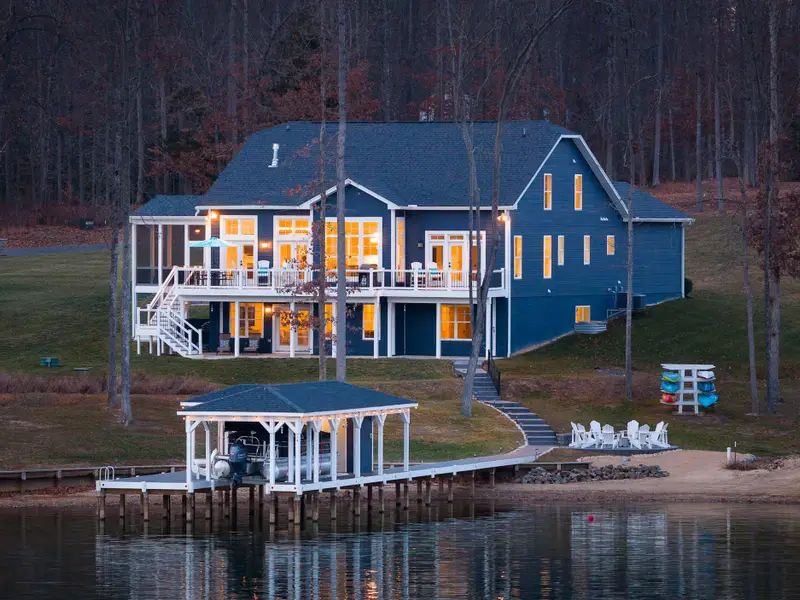 Exterior - From the dock looking toward the house, warm interior light and the covered boathouse reflect on the still water.