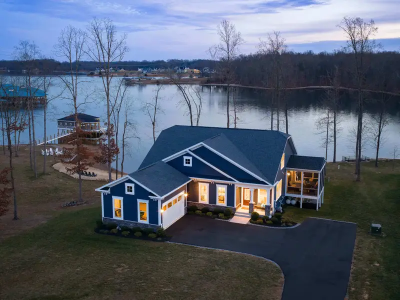 Exterior - A twilight aerial from above shows the front of the house and screened porch glowing, with the boathouse lit behind.