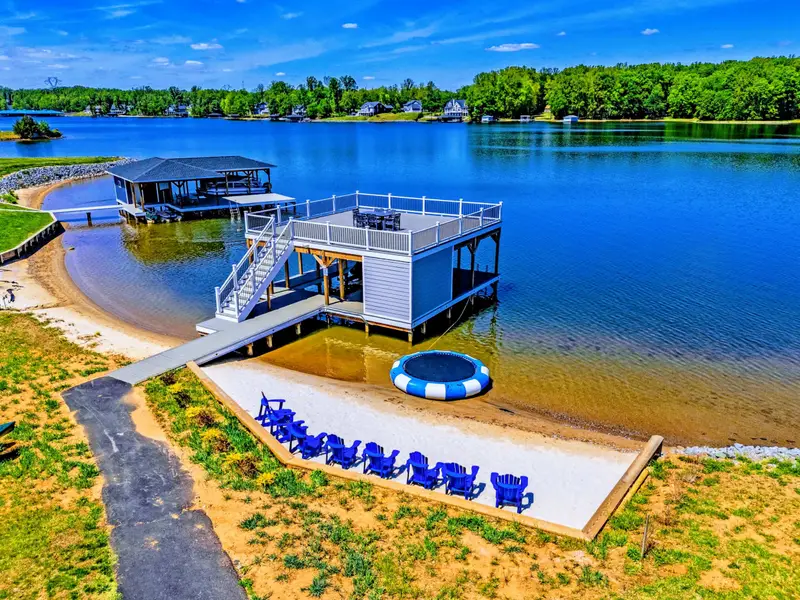 Backyard & Beach - Closer look at the lakefront setup: beach loungers, floating water trampoline, two-story dock for shaded gatherings.
