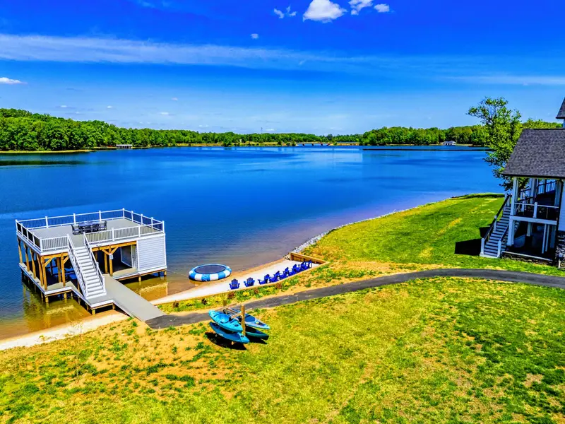 Backyard & Beach - Wide view from across the cove. Kayaks staged on the lawn, beach chairs in line, dock above the water.