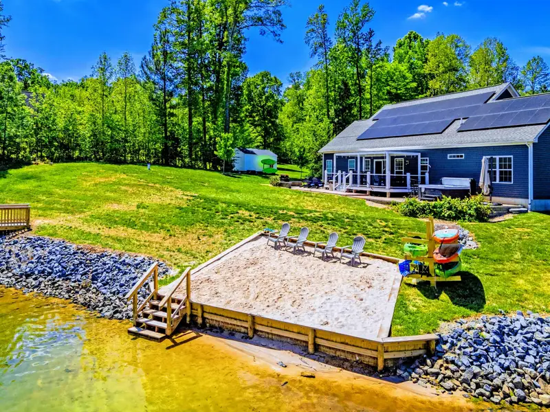 Aerial - The view from the water: private sandy beach below, retaining walls, and the blue craftsman home set above.