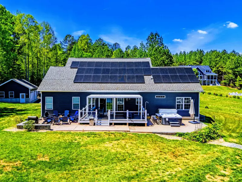 Aerial - Back-of-house from above: covered porch, dining deck, fire pit patio, and lakeside hot tub all in one frame.