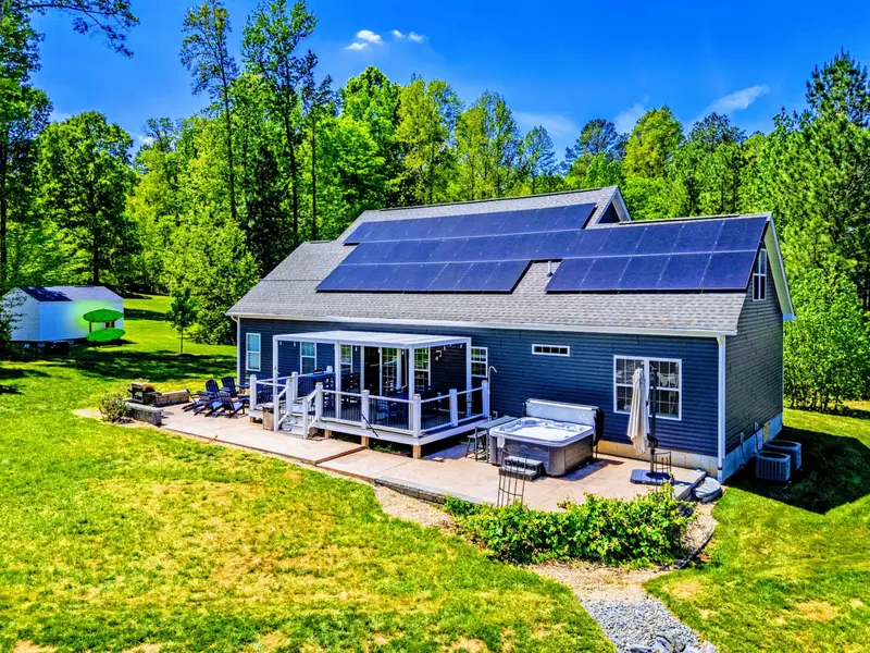 Aerial - Side view of the home with the hot tub patio, deck, and fire pit lounge stretched across the back.