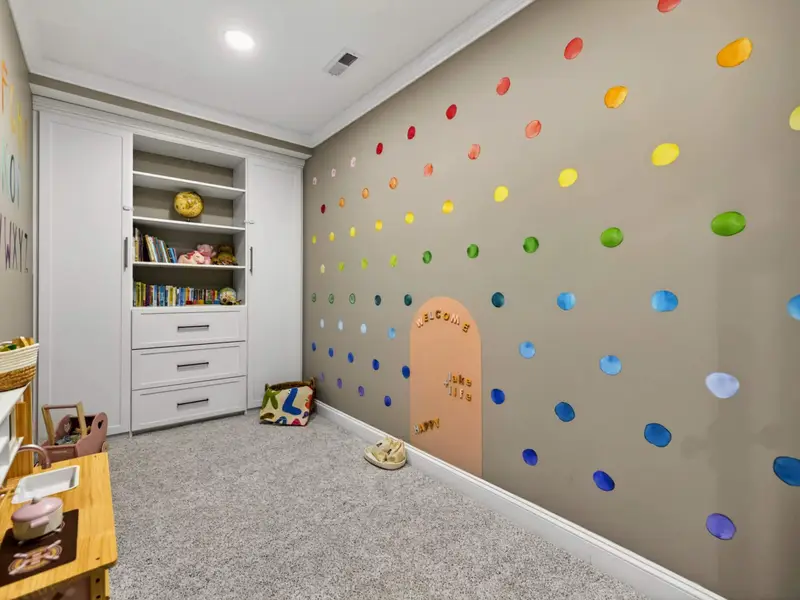 Children's Playroom - Built-in shelving stocked with books and a polka-dot climbing wall on the opposite side, two activities in one cozy room.