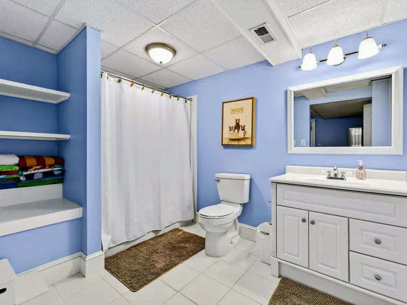 Lower Bath - A bright blue lower-level bathroom with full tub-shower, white vanity, and plenty of storage.
