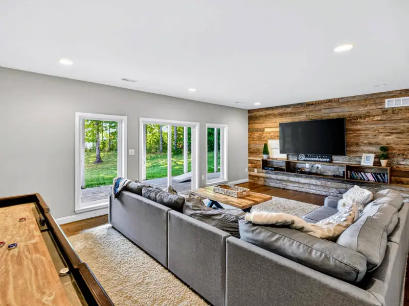 A spacious lower-level family room with a large sectional, mounted TV on a reclaimed-wood accent wall, and a shuffleboard table just off the seating area.