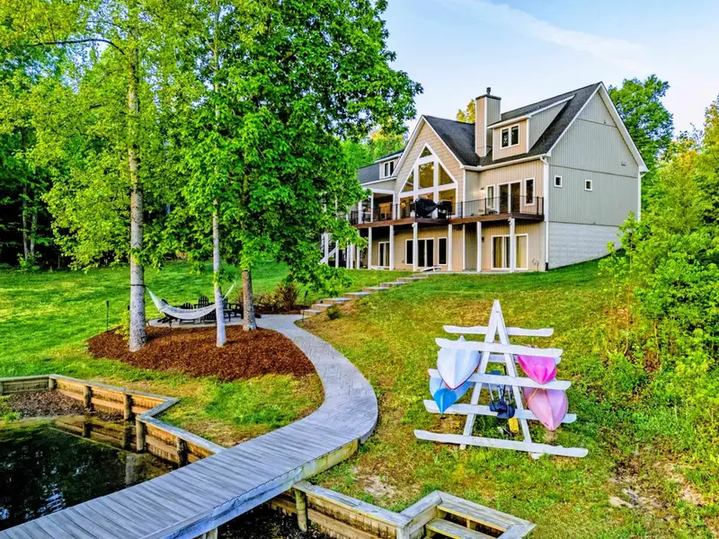 A scenic backyard view of the home featuring a colorful kayak rack, a shaded hammock, and a walkway leading down to the private dock.