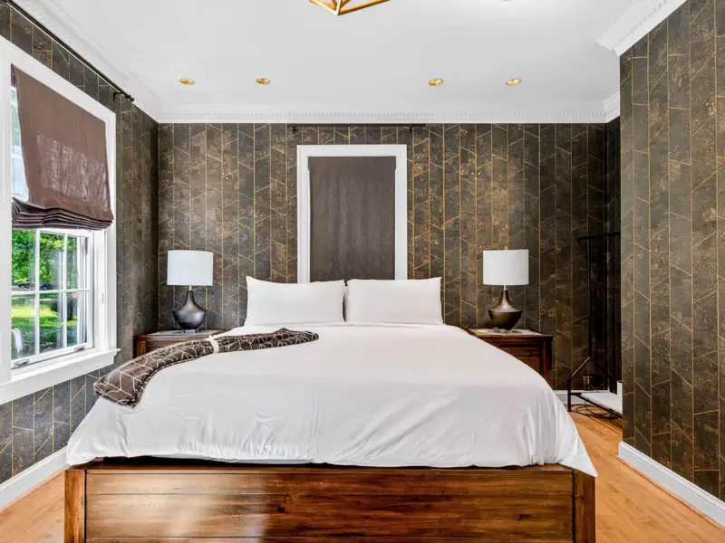 King Bedroom - Dark wallpapered accent with king bed and warm wood floors.