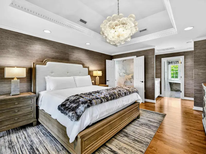 Primary Suite - Tray ceiling, statement chandelier, and a king bed against textured wallpaper.